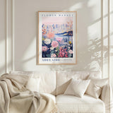 a framed poster of a flower market in Melbourne, Australia, hanging on a wall above a white couch with a blanket draped over it.