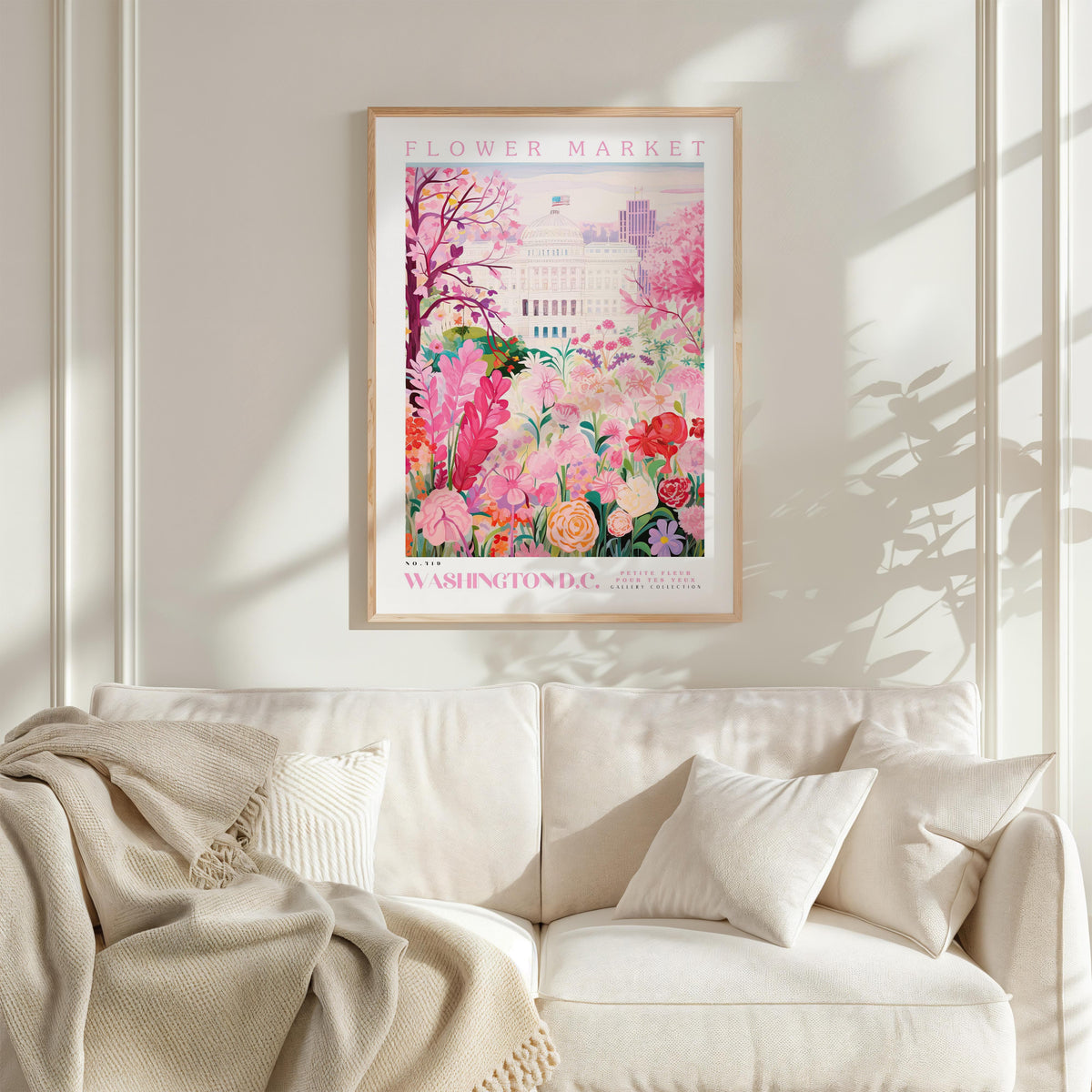 a framed poster of a colorful floral scene hanging on a wall above a white couch with a blanket draped over it.