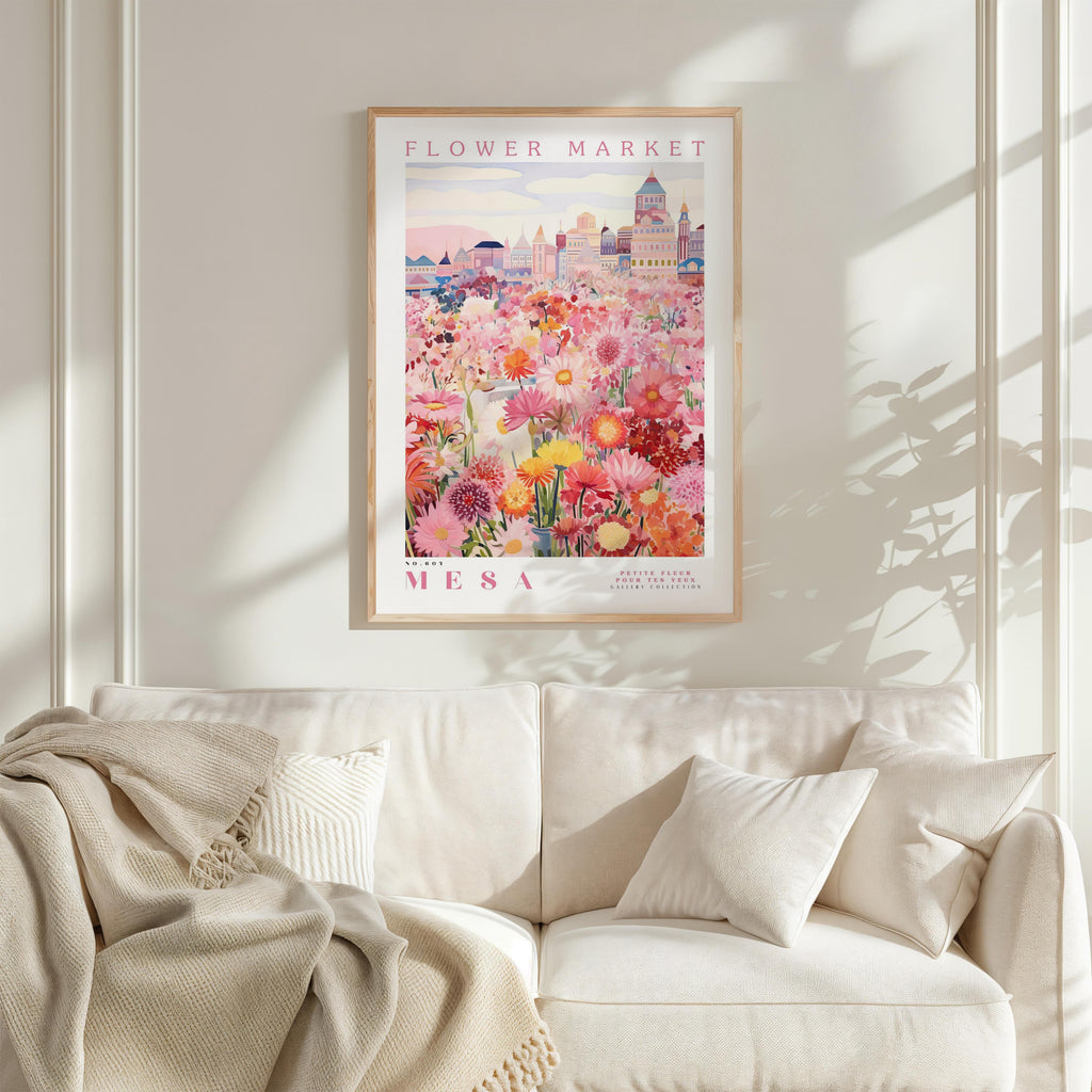 a framed poster of a vibrant floral scene hanging on a wall above a white couch with a blanket draped over it.