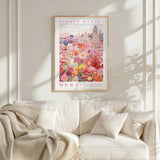 a framed poster of a vibrant floral scene hanging on a wall above a white couch with a blanket draped over it.