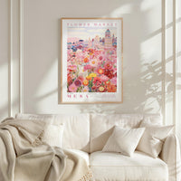 a framed poster of a vibrant floral scene hanging on a wall above a white couch with a blanket draped over it.
