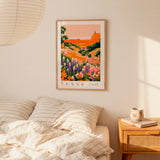 a bedroom scene with a framed poster of a colorful landscape hanging on the wall above a bed with striped pillows.