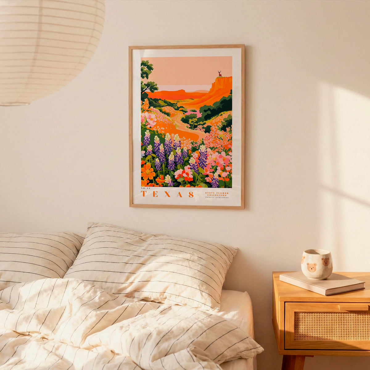 a bedroom scene with a framed poster of a colorful landscape hanging on the wall above a bed with striped pillows.