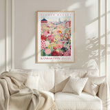 a framed poster of a colorful floral scene hanging on a wall above a white couch with a blanket draped over it.