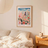 a bedroom setting with a framed poster of a cityscape and flowers hanging on the wall above a bed with striped pillows.