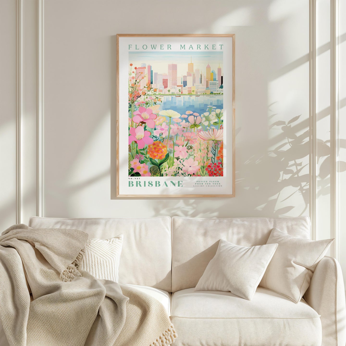 a framed poster of a cityscape with a flower market in the background, hanging on a wall above a white couch with a blanket draped over it.