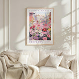 a framed poster of a colorful floral scene hanging on a wall above a white couch with a blanket draped over it.