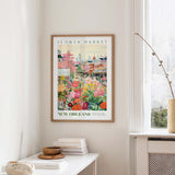 a framed poster of a colorful, vibrant flower market scene in New Orleans, with a cityscape visible in the background.