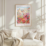 a framed poster of a colorful floral scene hanging on a wall above a white couch with a blanket draped over it.