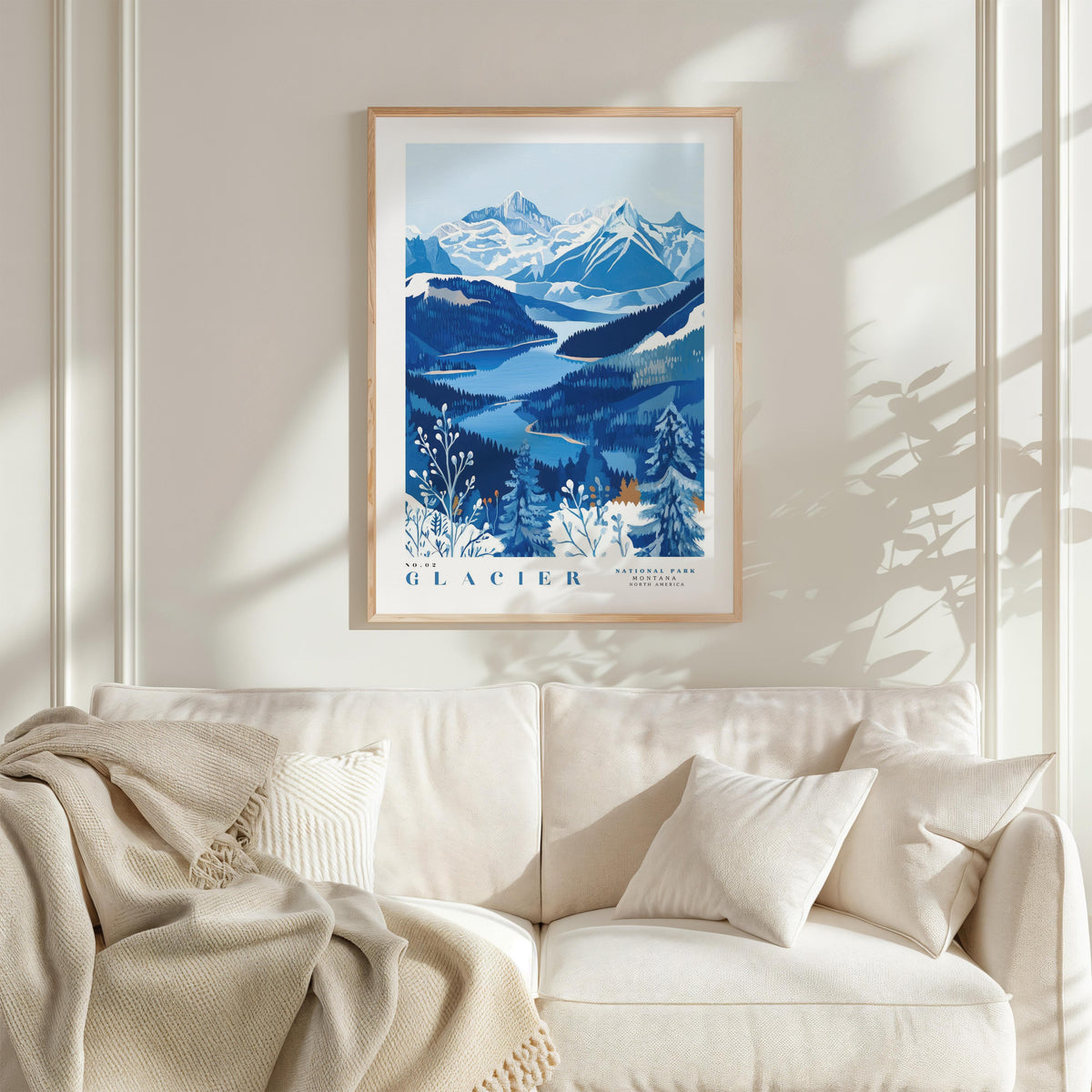 a framed poster of a mountainous landscape with a blue and white color scheme, hanging on a wall above a white couch with a blanket draped over it.