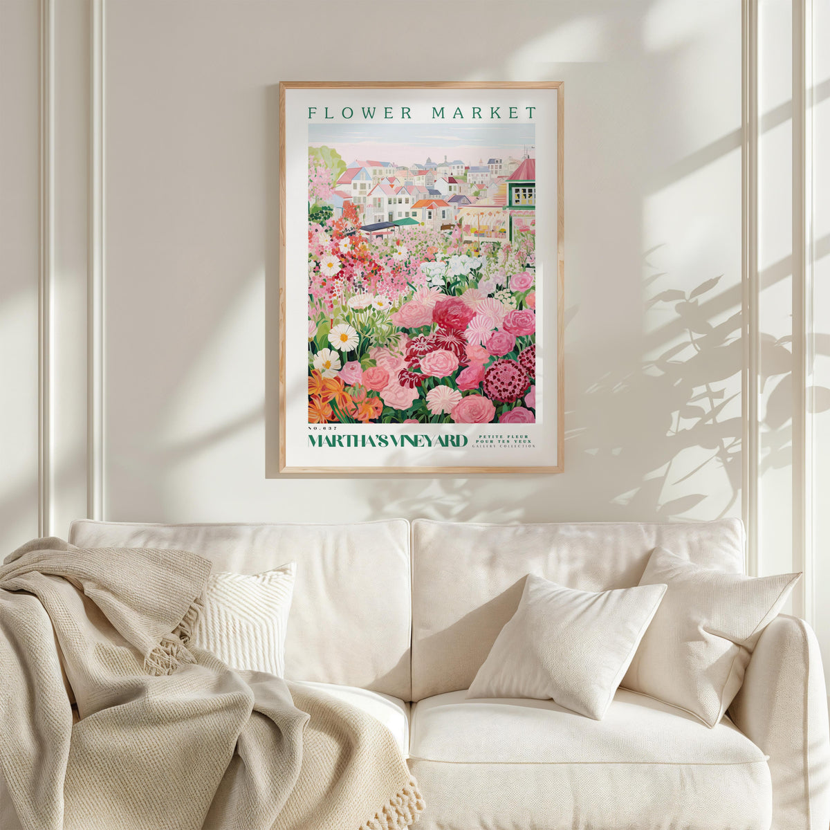 a framed poster of a flower market, hanging on a wall above a white couch with a blanket draped over it.