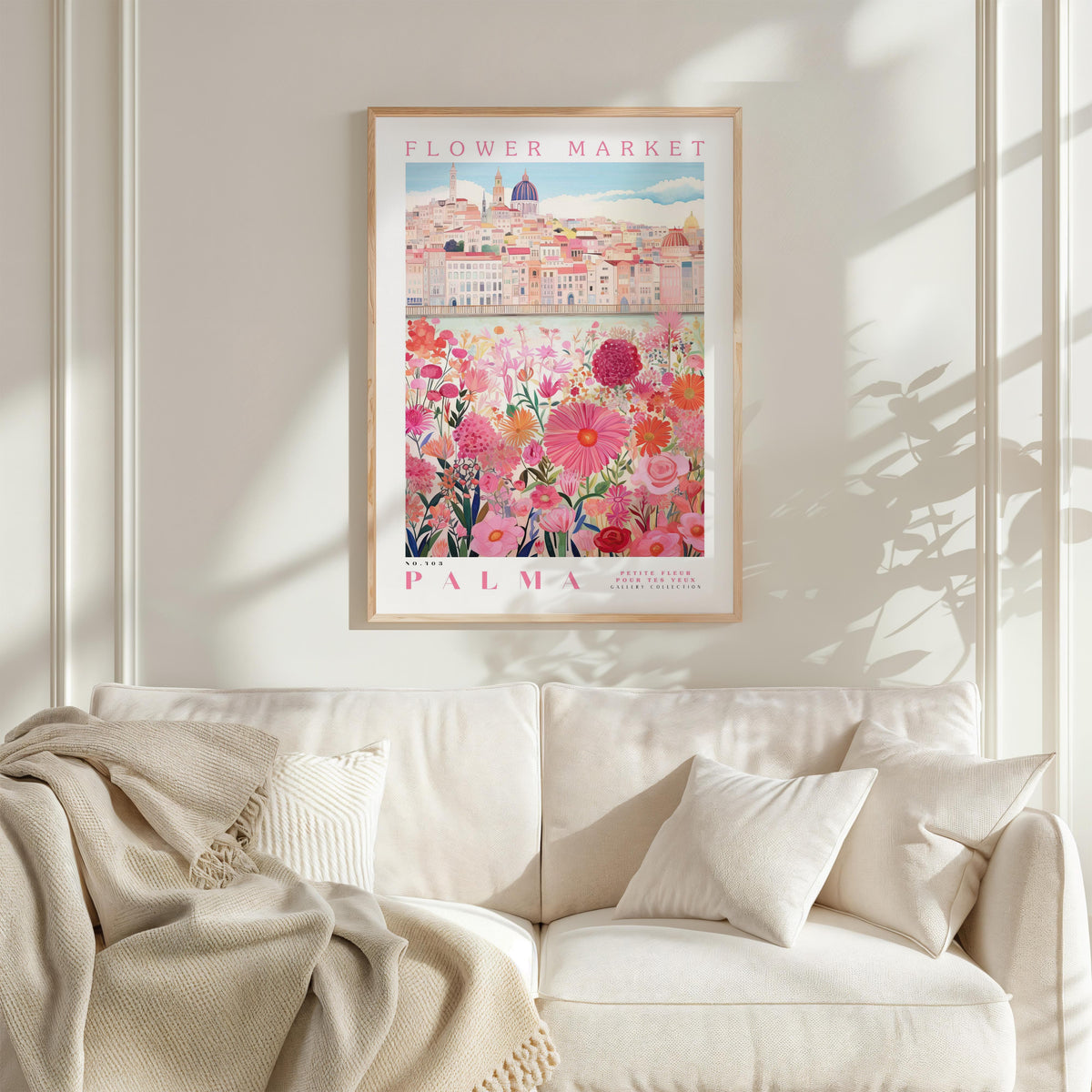 a framed poster of a cityscape with a field of flowers in the foreground, hanging on a wall above a white couch.