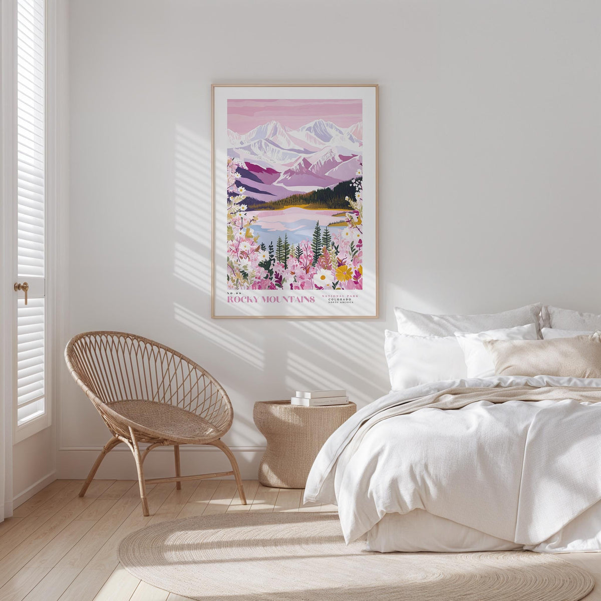 A bedroom with a large poster of a mountain landscape hanging on the wall, featuring a serene scene of mountains, trees, and a lake. The room has a white bed, a woven chair, and a wooden nightstand with a lamp.