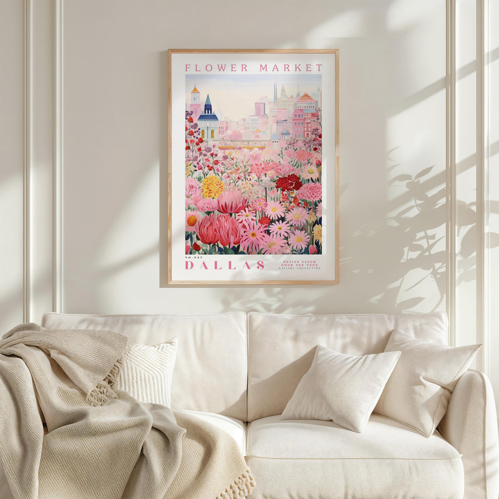 a framed poster of a flower market in Dallas, Texas, hanging on a wall above a white couch with a blanket draped over it.