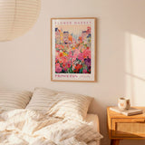 a bedroom scene with a framed poster of a colorful flower market hanging on the wall above a bed with striped pillows.