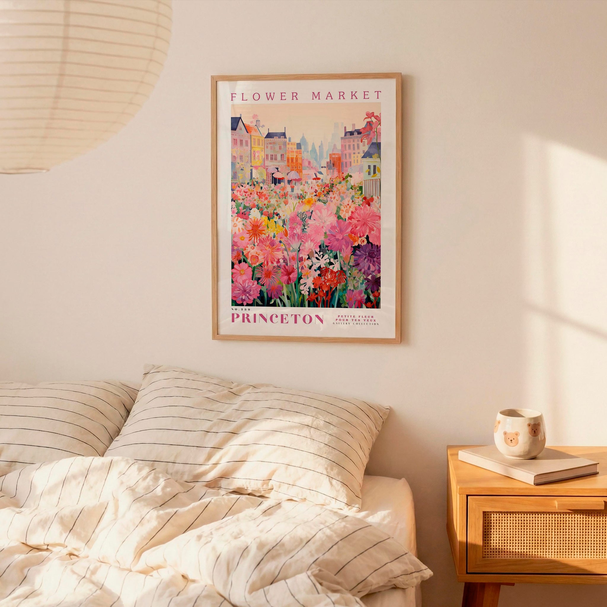 a bedroom scene with a framed poster of a colorful flower market hanging on the wall above a bed with striped pillows.