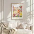 a framed poster of a colorful garden scene hanging on a wall above a white couch.