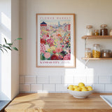 a framed poster of a colorful floral scene hanging on a wall above a kitchen counter with a bowl of lemons on it.