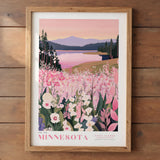 A framed poster depicting a scenic landscape with a lake, mountains, and a field of pink flowers.