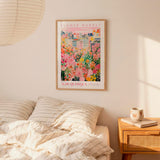 a bedroom setting with a framed poster of a colorful floral scene hanging on the wall above a bed with striped pillows.