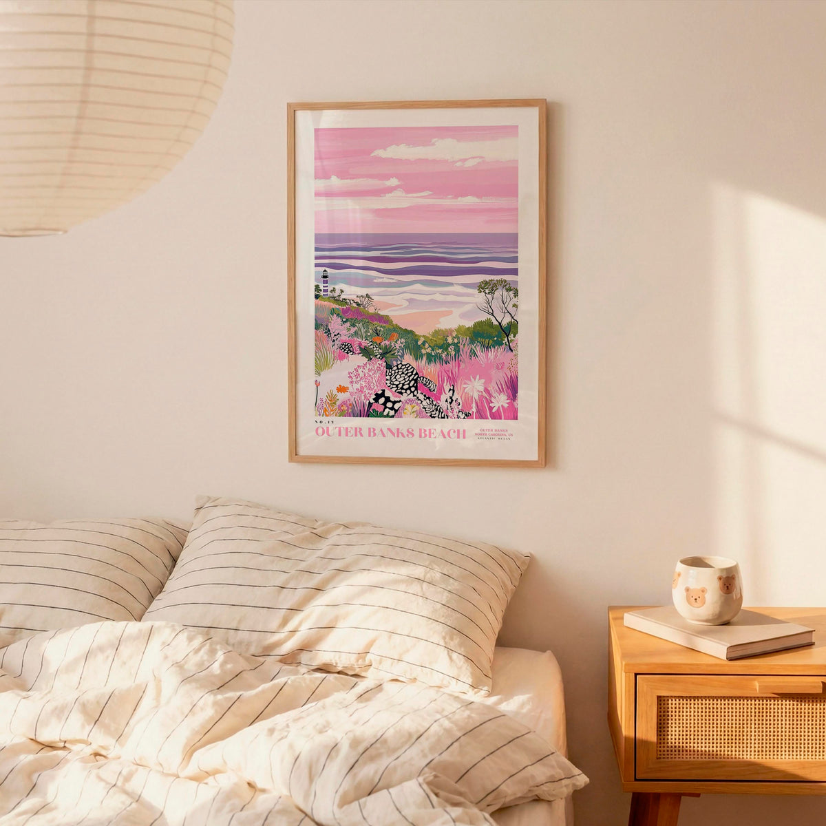 a bedroom scene with a framed poster of a beach landscape hanging on the wall above a bed with striped pillows.