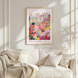 a poster of a flower market in a city, hanging on a wall above a white couch with a blanket draped over it.