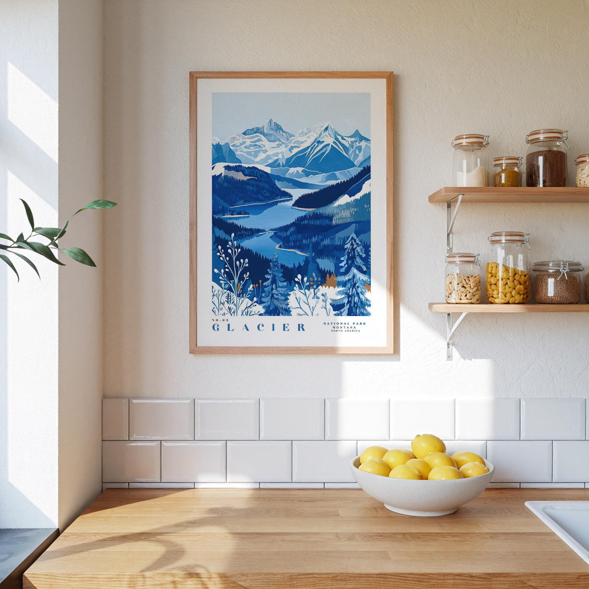 a framed poster of a mountainous landscape with a blue and white color scheme, hanging on a wall above a wooden countertop with a bowl of lemons.