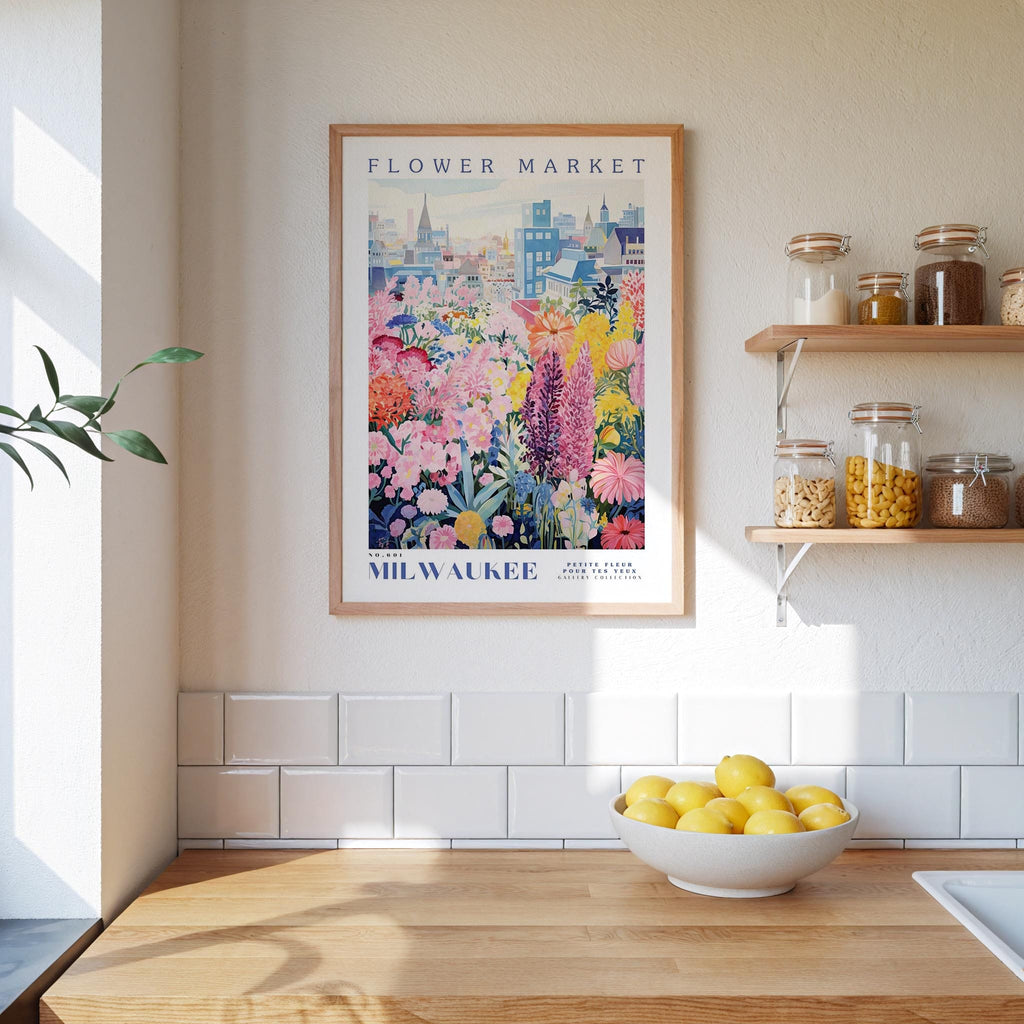 a framed poster of a colorful floral scene hanging on a wall above a kitchen counter with a bowl of lemons on it.