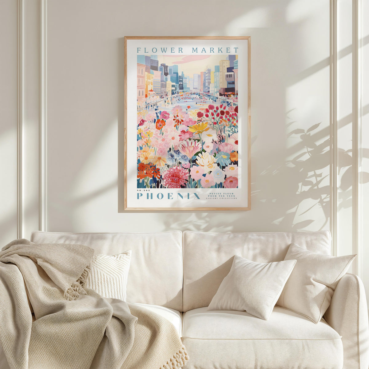 a framed poster of a colorful floral scene hanging on a wall above a white couch with a blanket draped over it.