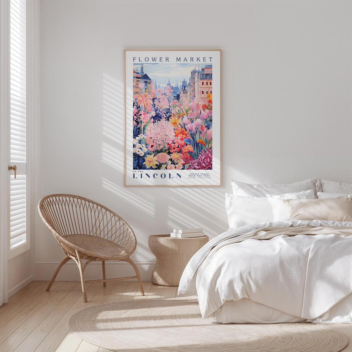 a bedroom with a bed, a woven chair, and a framed poster of a flower market in Lincoln, with a cityscape in the background.