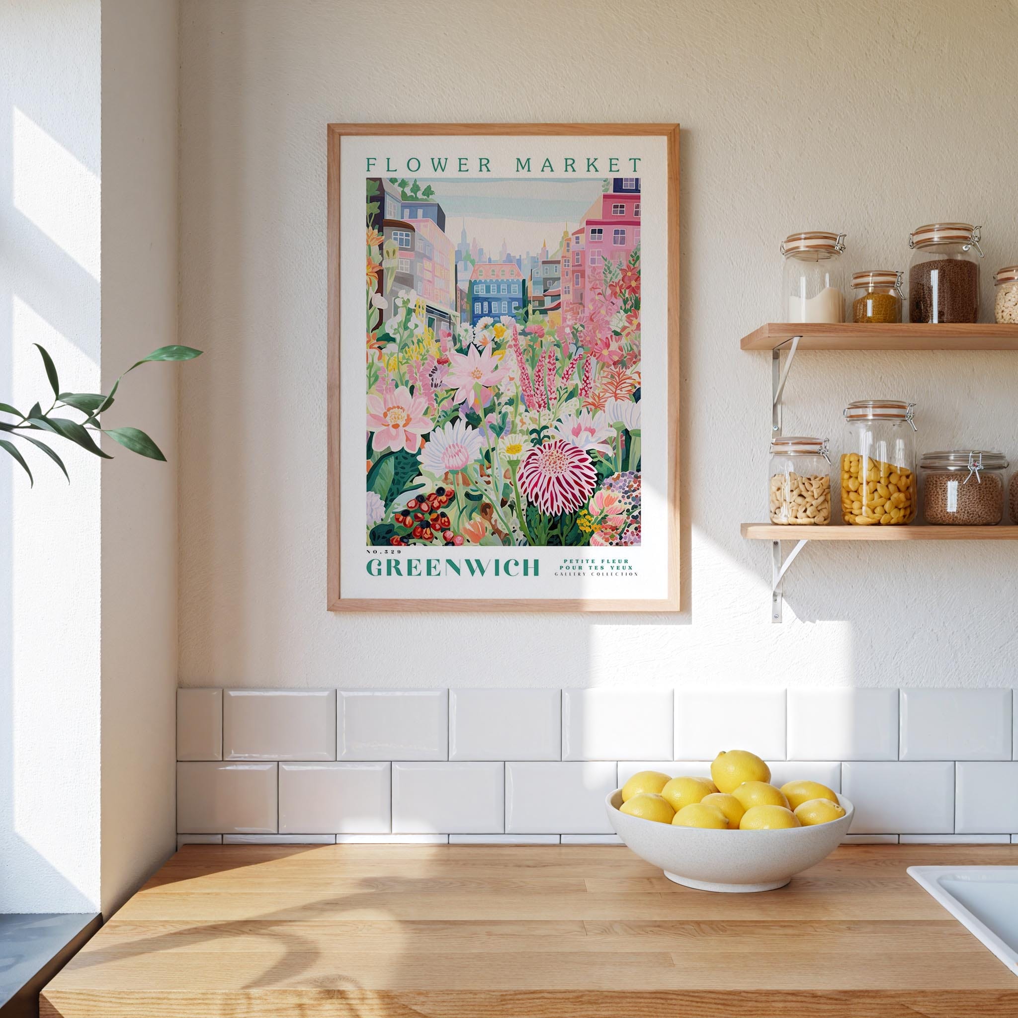a kitchen scene with a framed poster of a flower market in Greenwich, England, hanging on the wall above a wooden counter. The poster displays a colorful illustration of flowers and plants, and the text "FLOWER MARKET GREENWICH" is visible. On the counter, there is a bowl of lemons, and the wall has white tiles.