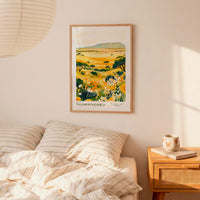 a bedroom scene with a framed print of a landscape depicting a field of flowers hanging on the wall above a bed with striped pillows.