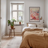 a cozy bedroom with a large bed, a nightstand with a potted plant, and a framed poster of a cityscape on the wall.