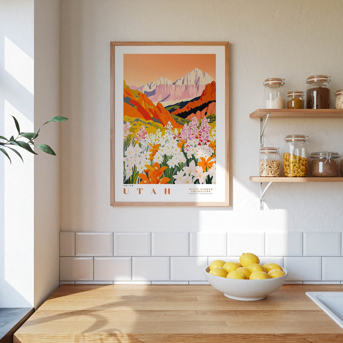 a kitchen counter with a bowl of lemons, a framed poster of a mountain landscape, and a shelf with jars and containers.