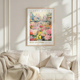 a framed poster of a colorful flower market in San Antonio, Texas, hanging on a wall above a white couch.