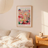 a bedroom scene with a framed poster of a colorful flower market in Kansas City hanging on the wall above a bed with striped pillows.