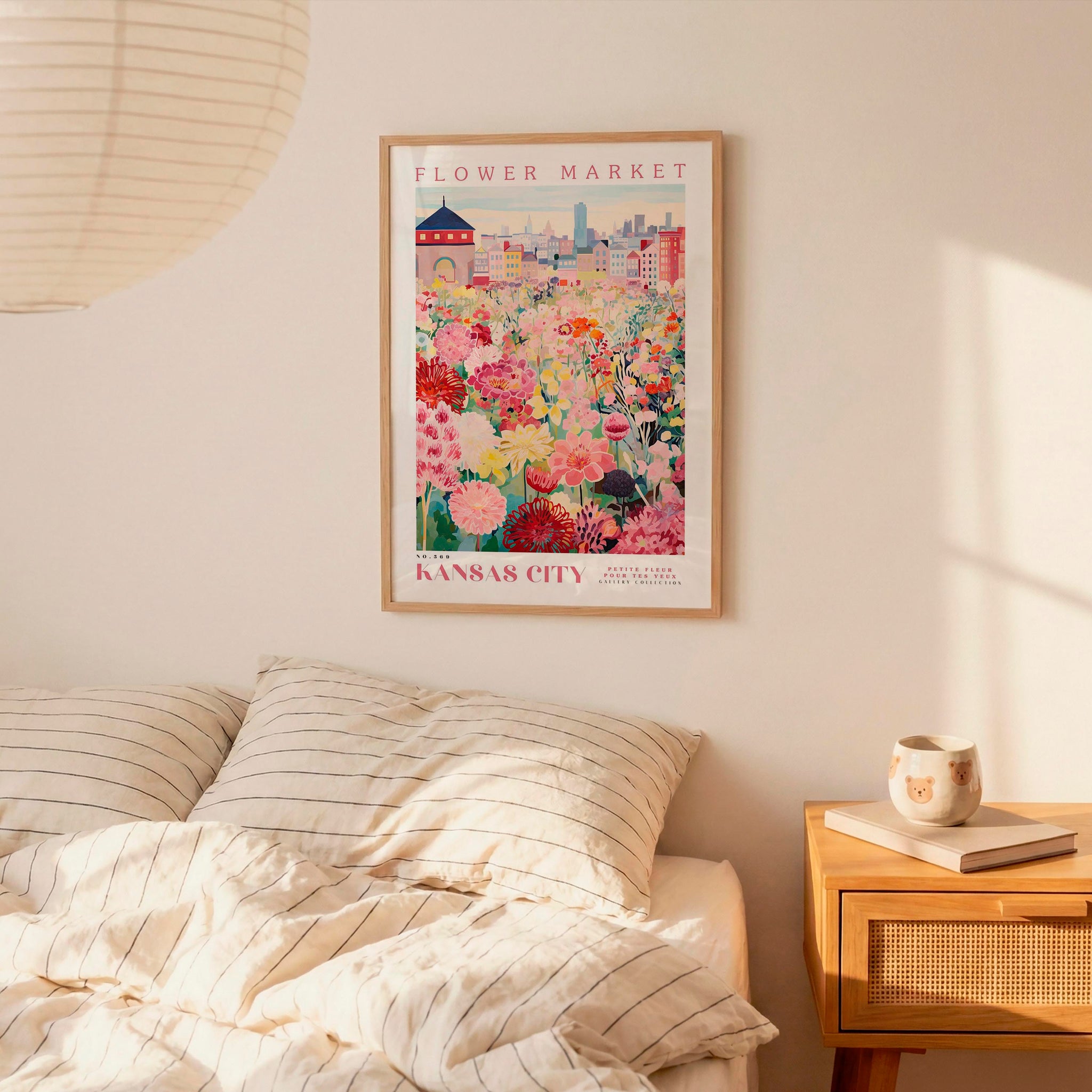 a bedroom scene with a framed poster of a colorful flower market in Kansas City hanging on the wall above a bed with striped pillows.