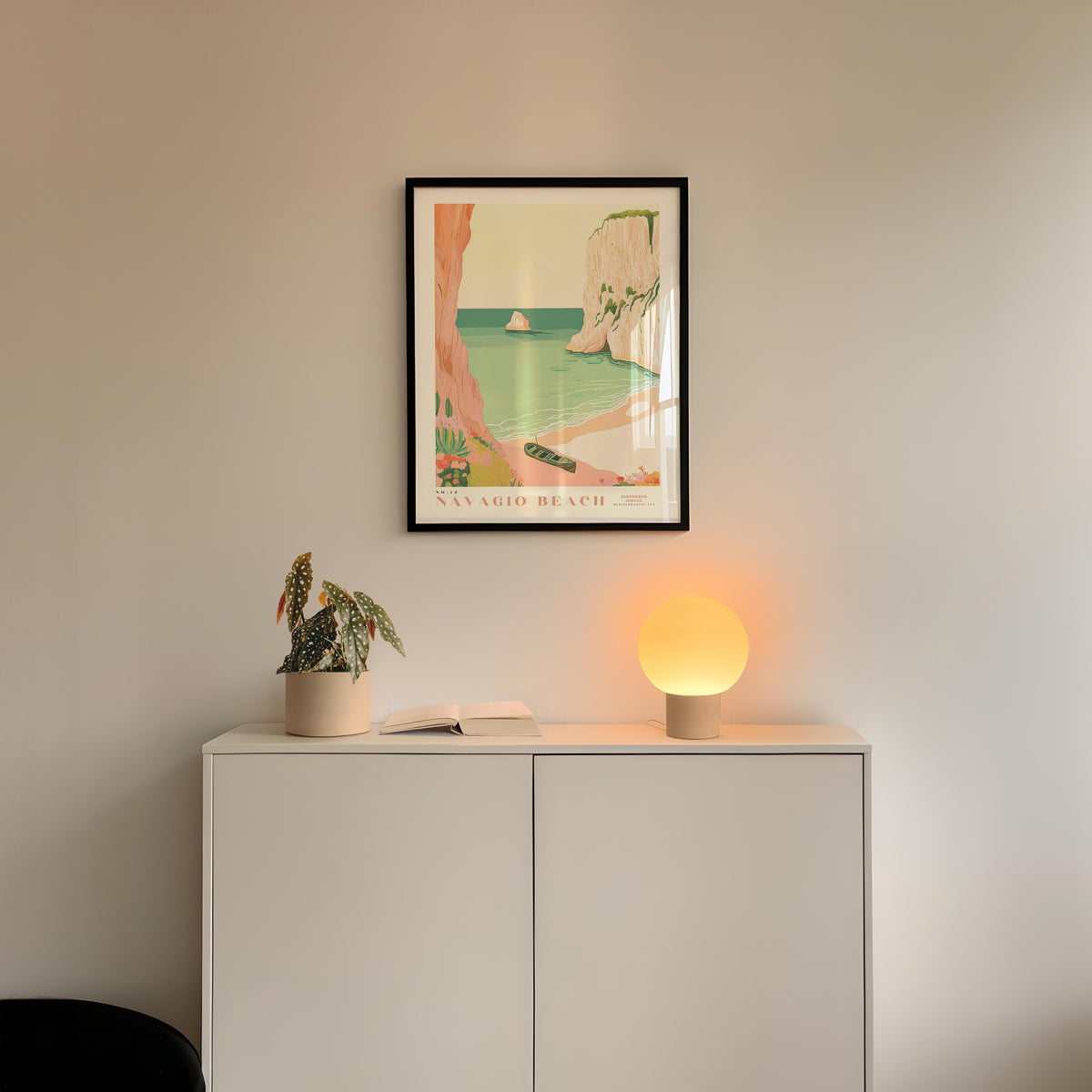 a white cabinet with a framed picture of a beach scene hanging above it, and a small lamp on the cabinet.