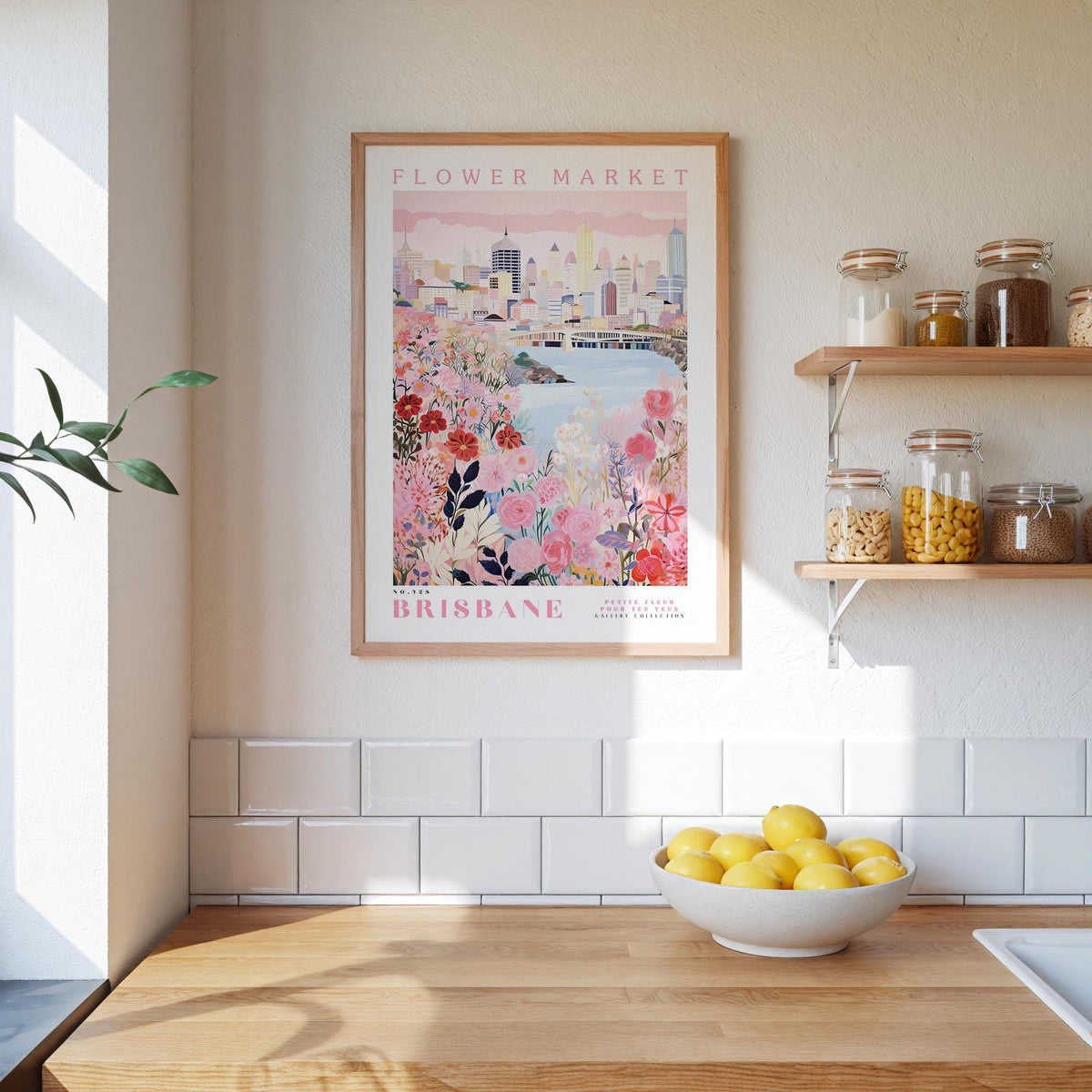 a framed poster of a cityscape with pink flowers, hanging on a wall above a wooden counter with a bowl of lemons.