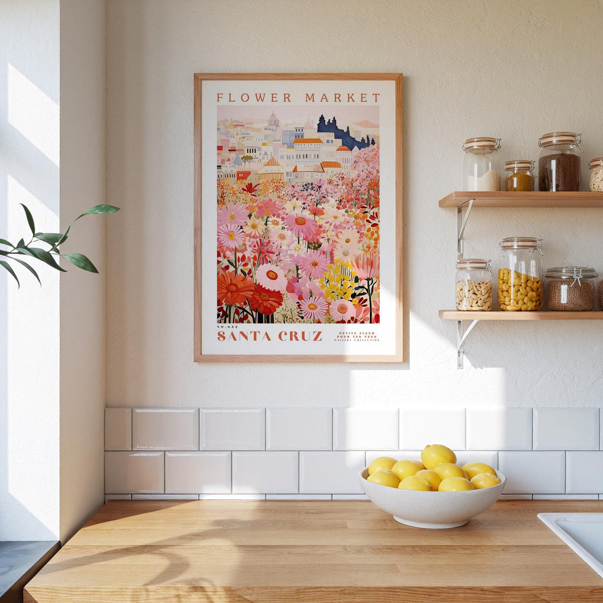 a framed poster of a colorful floral scene hanging on a wall above a kitchen counter with a bowl of lemons on it.