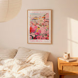 a bedroom setting with a framed poster of a colorful floral scene hanging on the wall above a bed with striped pillows.