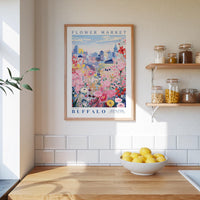 a framed poster of a cityscape with a flower market in the background, hanging on a wall above a kitchen counter with a bowl of lemons.