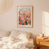 a framed poster of a colorful flower market in Las Vegas, with a bed and a nightstand in the foreground.