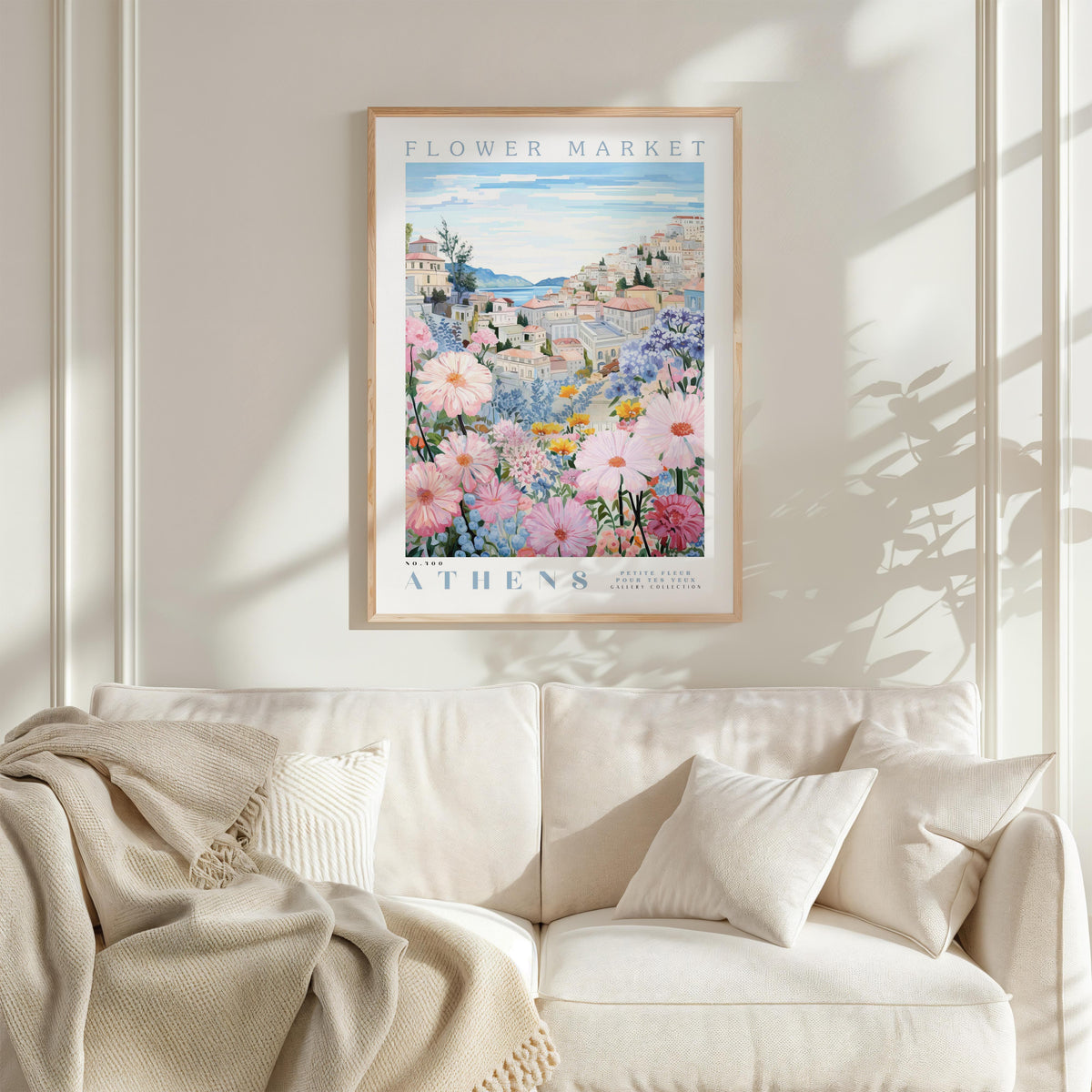 a framed poster of a flower market in Athens, Greece, hanging on a wall above a white couch with a blanket draped over it.