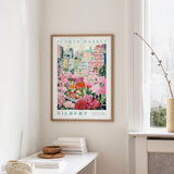 a framed poster of a colorful garden scene with flowers hanging on a wall in a room.