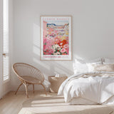a bedroom with a bed, a woven chair, and a framed poster of a flower market.