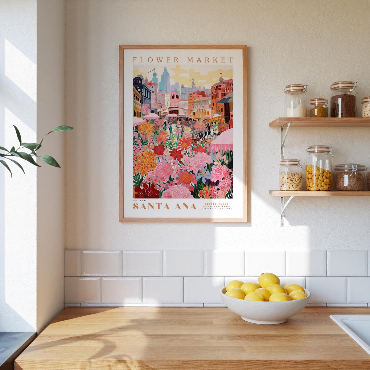 a framed poster of a colorful illustration of a flower market in Santa Ana, California, hanging on a wall above a kitchen counter with a bowl of lemons and jars of food.