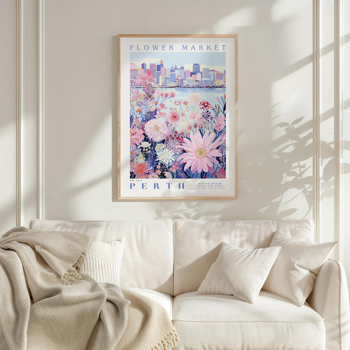 a framed poster of a cityscape with a flower market in the background, hanging on a wall above a white couch with a blanket draped over it.
