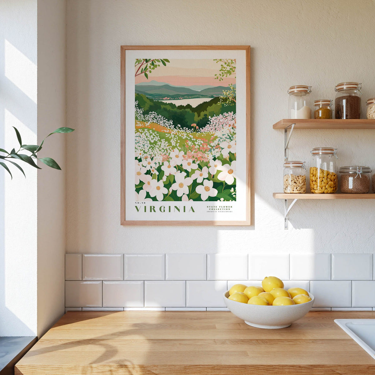 a framed poster of a garden with white flowers hanging on a wall above a wooden table with a bowl of lemons.