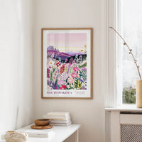 a framed poster of a colorful floral landscape hanging on a wall, with a white table and a vase of flowers in the foreground.